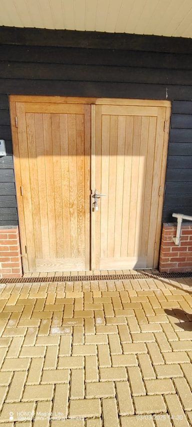 Wooden double doors with a lock, set against a dark wall and paved ground.